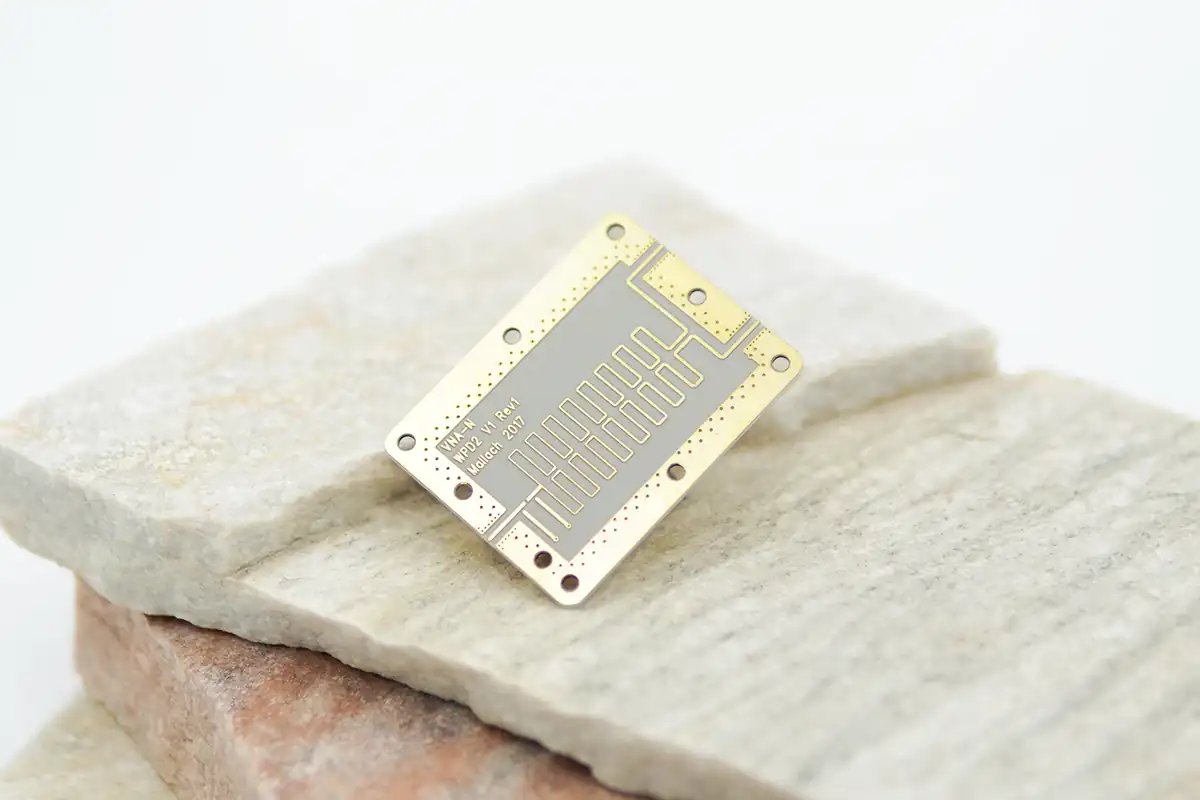 A small, intricately designed PCB (printed circuit board) with gold and silver detailing, placed on a stack of stone slabs.